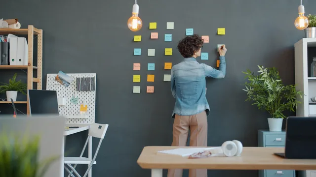 Woman planning with sticky notes on wall in modern office setting. Rengøringsaftaler til virksomheder: behov, kvalitet og opfølgning